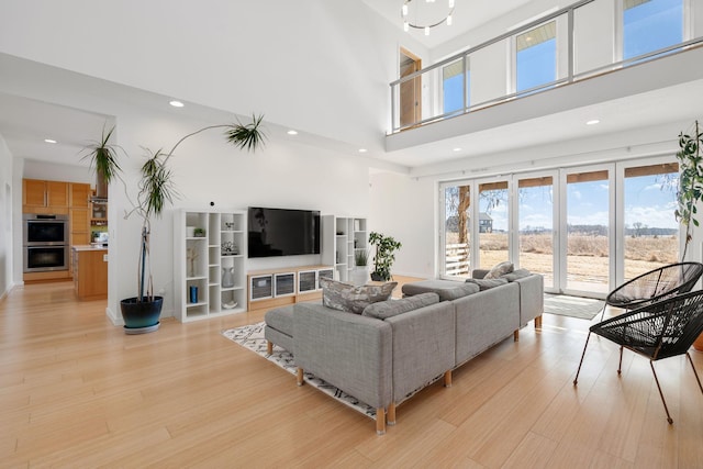 living room with light wood-type flooring, a high ceiling, baseboards, and recessed lighting