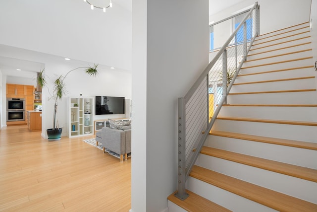 stairs featuring recessed lighting, a high ceiling, wood finished floors, and a glass covered fireplace