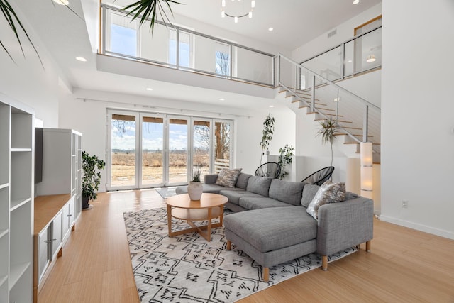 living room with recessed lighting, light wood-style flooring, a high ceiling, baseboards, and stairs