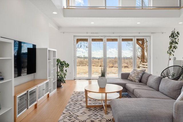 living room with a healthy amount of sunlight, light wood-style flooring, a towering ceiling, and recessed lighting