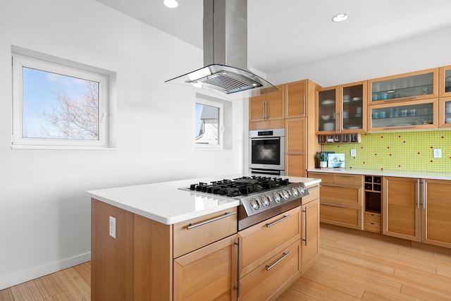 kitchen with light wood-style flooring, stainless steel appliances, tasteful backsplash, island exhaust hood, and glass insert cabinets