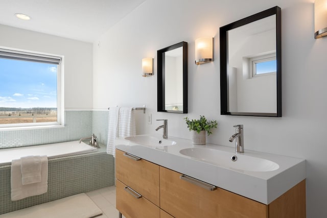 bathroom with a relaxing tiled tub, a sink, and double vanity