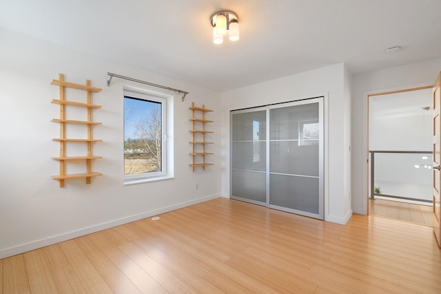 unfurnished bedroom featuring light wood-style flooring, baseboards, and a closet