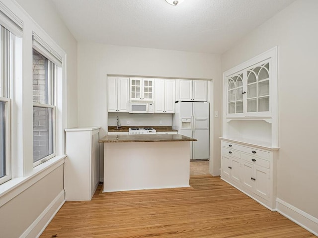 kitchen with white appliances, kitchen peninsula, white cabinets, light hardwood / wood-style flooring, and sink