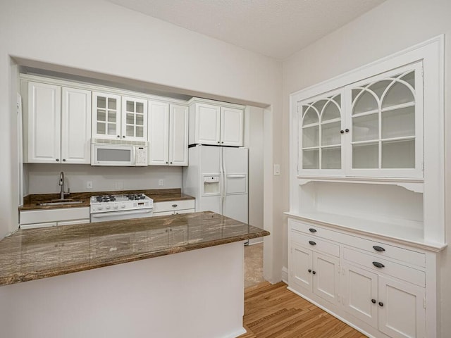 kitchen featuring sink, white cabinetry, white appliances, light hardwood / wood-style floors, and dark stone counters