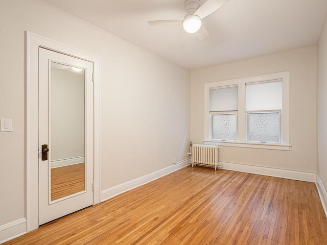 empty room featuring light wood-type flooring, ceiling fan, and radiator heating unit