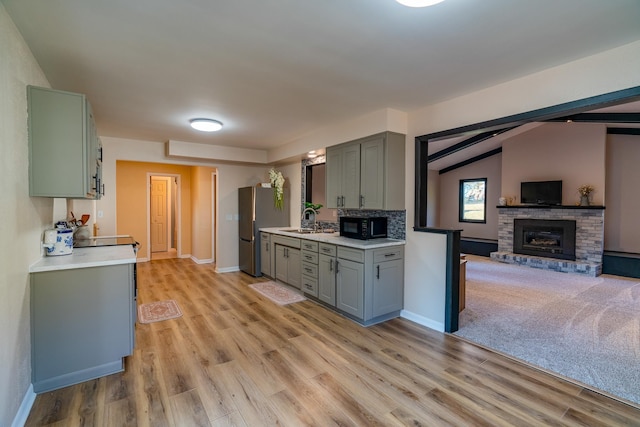 kitchen featuring vaulted ceiling with beams, a brick fireplace, light wood-type flooring, and stainless steel refrigerator