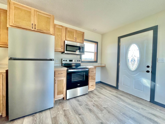 kitchen featuring light hardwood / wood-style floors, stainless steel appliances, light brown cabinetry, and a textured ceiling