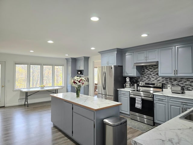 kitchen featuring dark wood-type flooring, gray cabinetry, a center island, appliances with stainless steel finishes, and tasteful backsplash