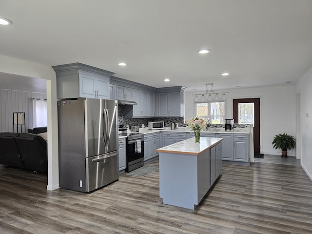 kitchen with gray cabinetry, appliances with stainless steel finishes, wood-type flooring, and a kitchen island