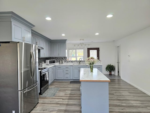 kitchen featuring decorative backsplash, appliances with stainless steel finishes, wood-type flooring, gray cabinets, and sink