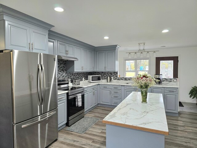 kitchen featuring decorative backsplash, gray cabinetry, stainless steel appliances, hardwood / wood-style floors, and light stone counters