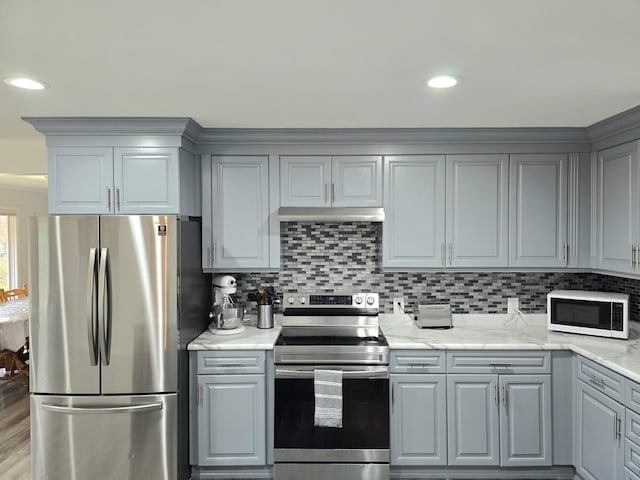 kitchen featuring light stone countertops, appliances with stainless steel finishes, backsplash, hardwood / wood-style floors, and gray cabinets