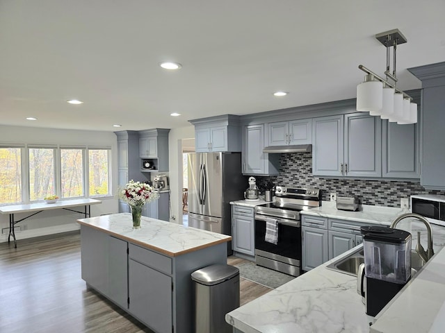 kitchen with a kitchen island, wood-type flooring, backsplash, gray cabinets, and appliances with stainless steel finishes