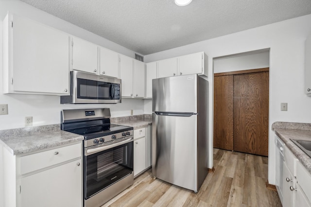 kitchen with a textured ceiling, appliances with stainless steel finishes, light hardwood / wood-style flooring, and white cabinets