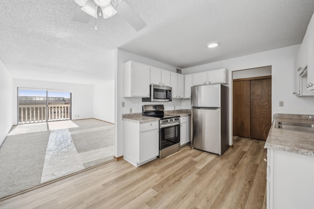 kitchen featuring appliances with stainless steel finishes, white cabinetry, light wood-type flooring, and ceiling fan