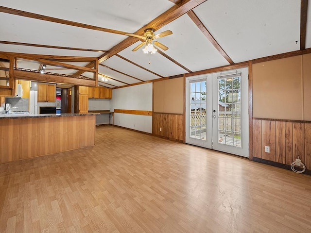 unfurnished living room with french doors, light hardwood / wood-style flooring, lofted ceiling with beams, ceiling fan, and wood walls