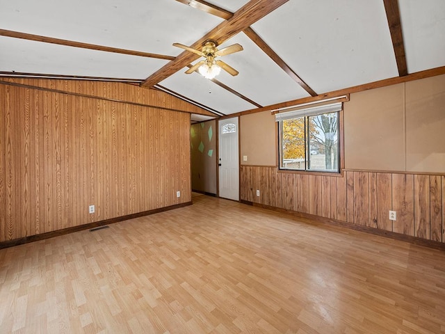 spare room with wooden walls, vaulted ceiling with beams, and light hardwood / wood-style floors