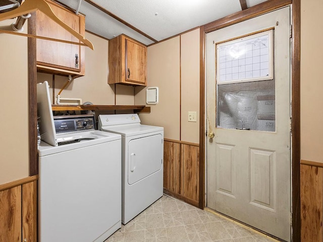 laundry room featuring wood walls, a textured ceiling, cabinets, and washing machine and clothes dryer