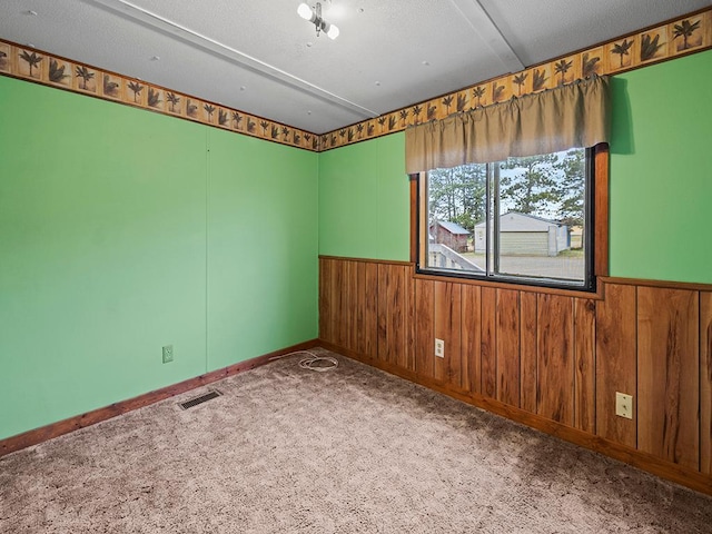 carpeted empty room with wood walls and a textured ceiling