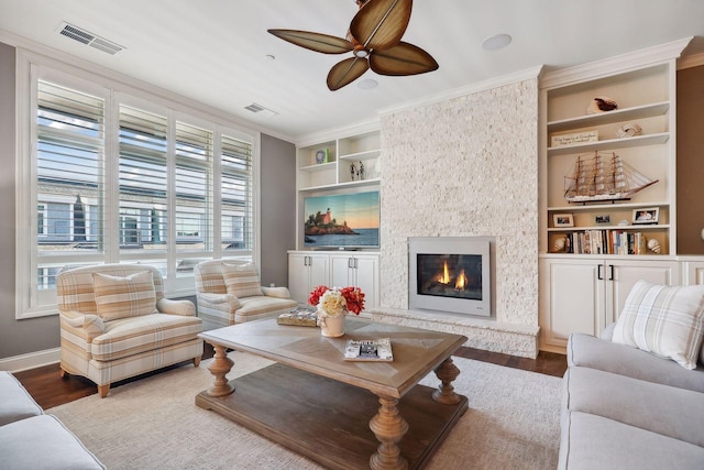 living room with ceiling fan, built in features, ornamental molding, a fireplace, and hardwood / wood-style flooring