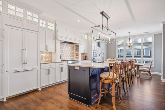 kitchen featuring white cabinetry, pendant lighting, custom range hood, and a center island with sink