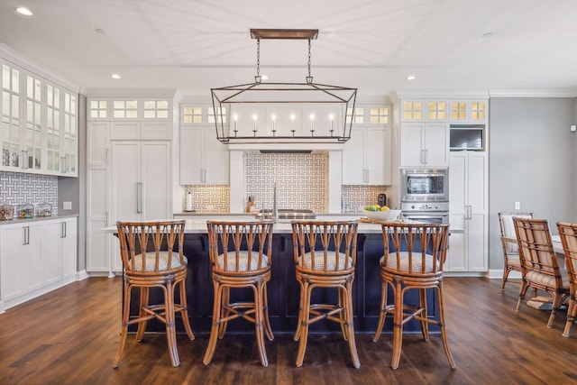 kitchen with pendant lighting, a kitchen island with sink, stainless steel microwave, and white cabinets