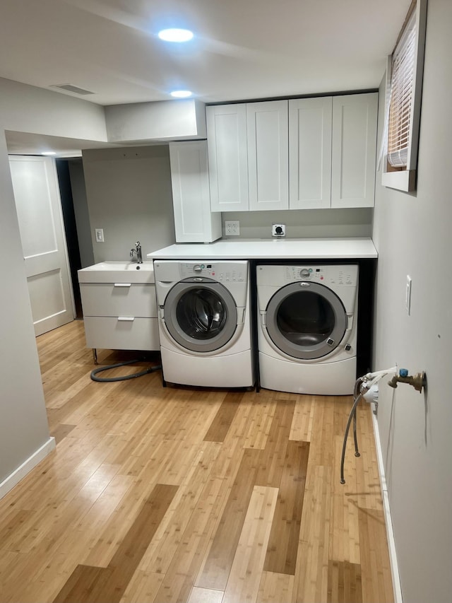 washroom with washer and clothes dryer, sink, light hardwood / wood-style floors, and cabinets