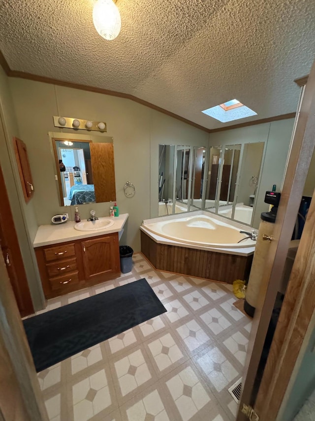 bathroom with ornamental molding, a textured ceiling, vaulted ceiling with skylight, vanity, and a washtub