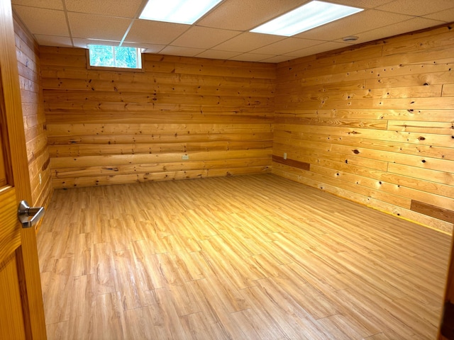 spare room featuring wood walls, a drop ceiling, and light wood-type flooring