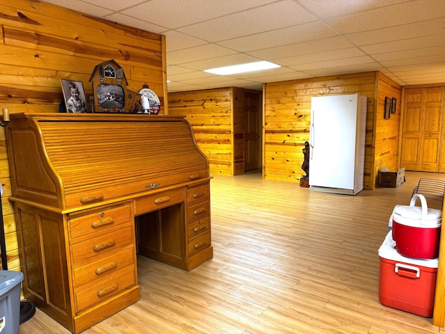 interior space featuring a paneled ceiling, wooden walls, and light wood-type flooring