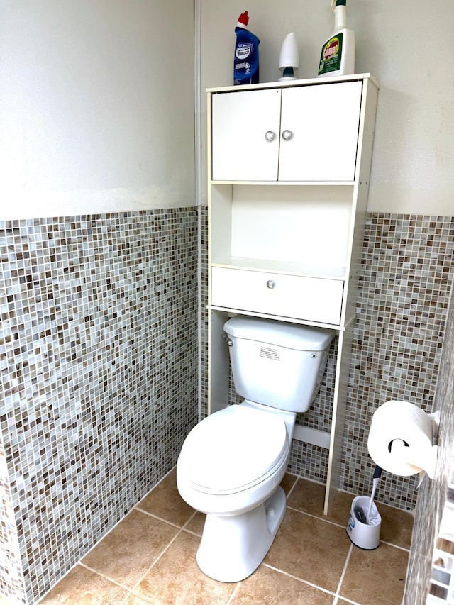 bathroom with toilet, tile patterned floors, and tile walls