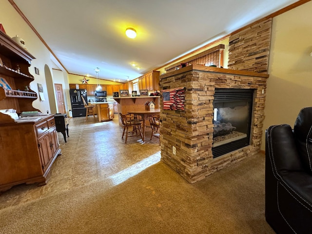 living room with crown molding, vaulted ceiling, a stone fireplace, and carpet