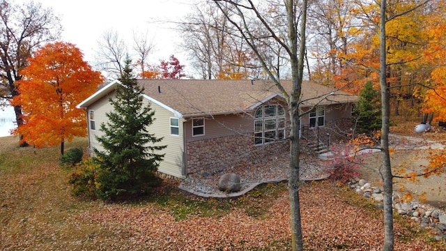 view of side of home featuring stone siding and a shingled roof