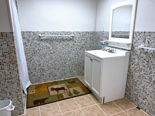 full bathroom with a wainscoted wall, a tile shower, tile walls, tile patterned flooring, and vanity