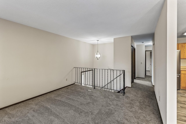 unfurnished room with dark carpet, a textured ceiling, and an inviting chandelier