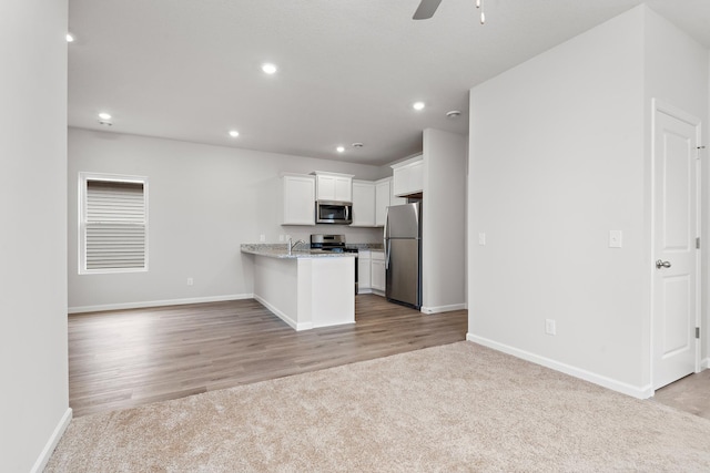 kitchen with kitchen peninsula, white cabinets, light wood-type flooring, appliances with stainless steel finishes, and light stone counters