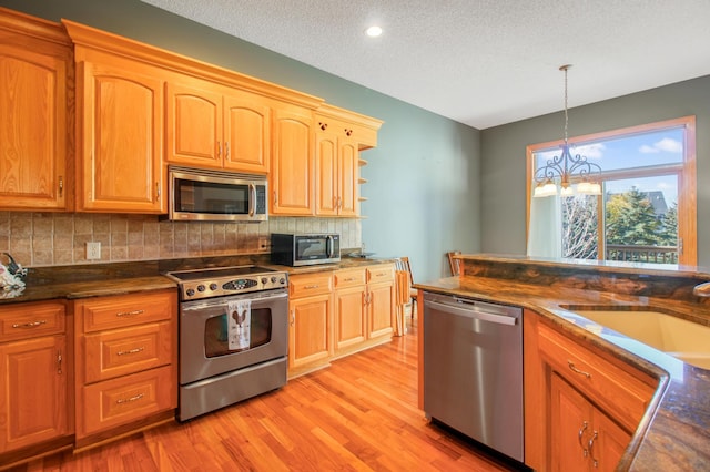 kitchen featuring stainless steel appliances, a textured ceiling, decorative light fixtures, a chandelier, and light hardwood / wood-style flooring