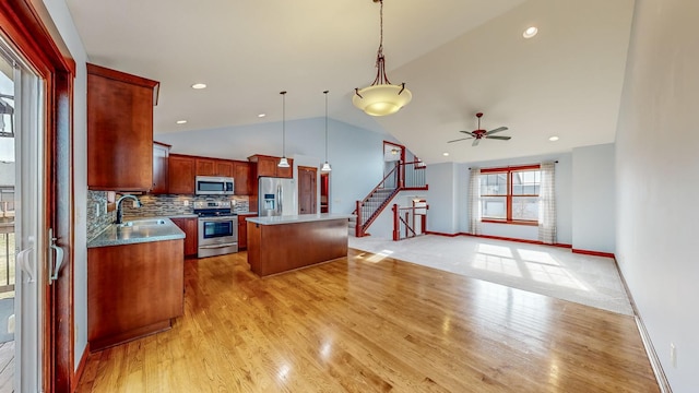 kitchen with lofted ceiling, hanging light fixtures, stainless steel appliances, sink, and a center island