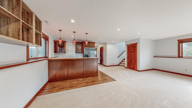 kitchen featuring hanging light fixtures, kitchen peninsula, light colored carpet, and stainless steel fridge