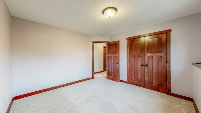 unfurnished bedroom with light carpet, a textured ceiling, and a closet