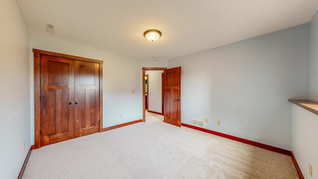 unfurnished bedroom with a closet, a textured ceiling, and light colored carpet