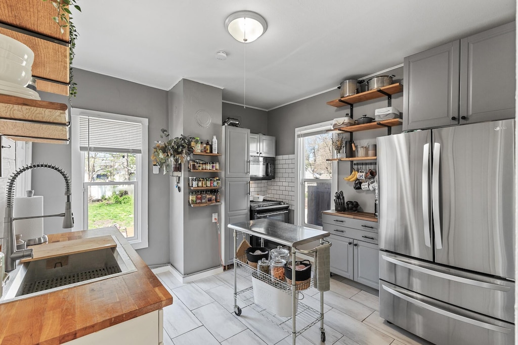 kitchen with tasteful backsplash, appliances with stainless steel finishes, wood counters, gray cabinets, and sink