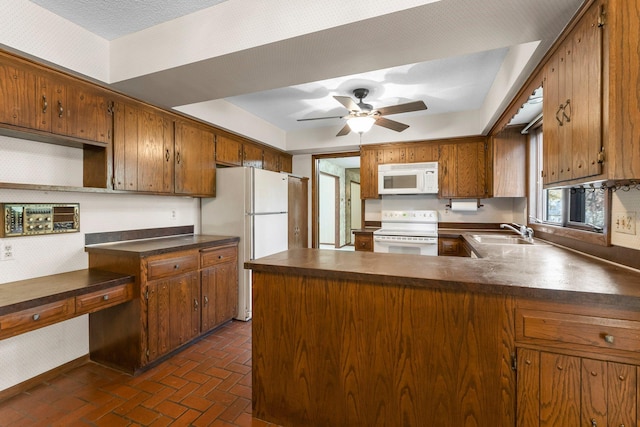 kitchen with white appliances, sink, a raised ceiling, kitchen peninsula, and ceiling fan