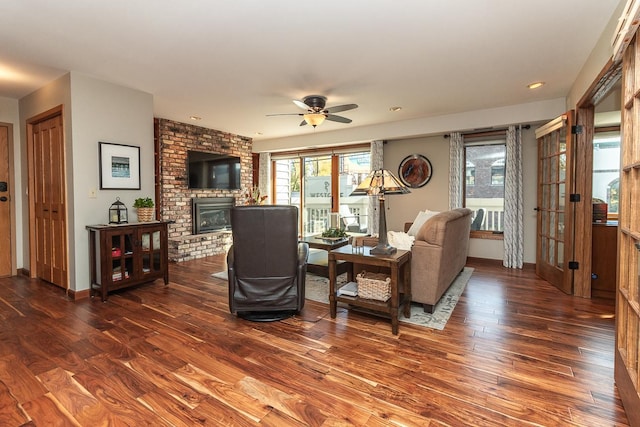 living room with a brick fireplace, wood finished floors, a ceiling fan, and baseboards