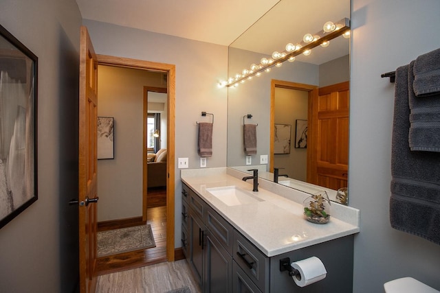 bathroom with ensuite bathroom, toilet, wood finished floors, vanity, and baseboards