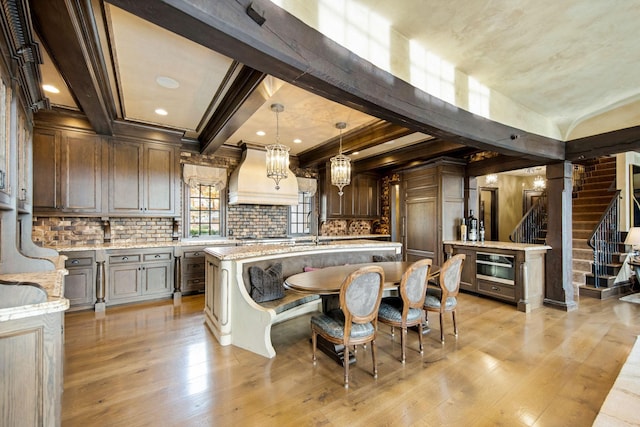 10675 Cavallo Rdg, Eden Prairie, MN 55347 - kitchen with custom range hood, light wood-style floors, tasteful backsplash, an island with sink, and pendant lighting