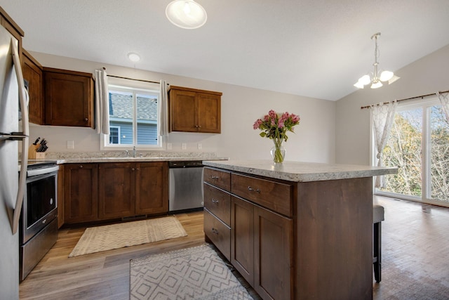 kitchen with appliances with stainless steel finishes, a center island, lofted ceiling, pendant lighting, and light hardwood / wood-style flooring