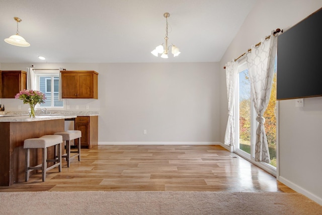 kitchen with vaulted ceiling, a breakfast bar area, light hardwood / wood-style flooring, and decorative light fixtures