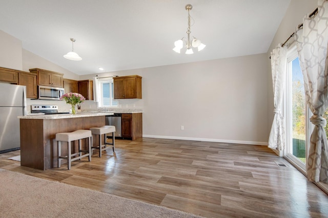 kitchen featuring a kitchen island, vaulted ceiling, decorative light fixtures, and stainless steel appliances